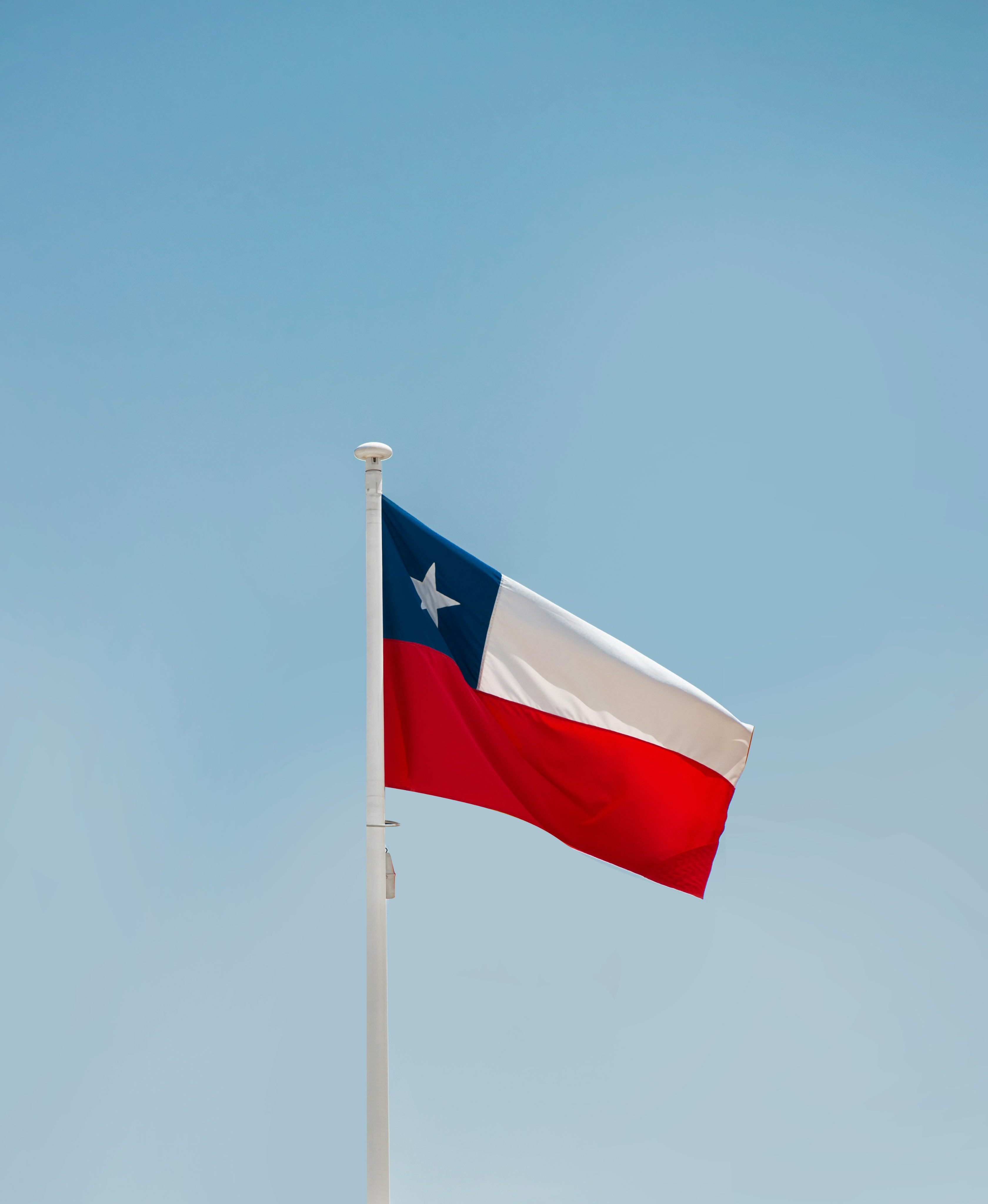 Texas state flag waving against a blue sky, representing Verde Landscape's proud Texas heritage and statewide service commitment
